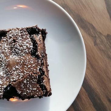 A piece of chocolate brownie dusted with powdered sugar on a white plate.