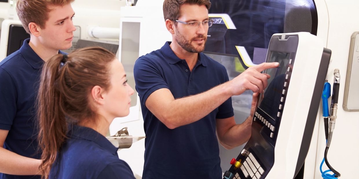 Instructor teaching students to operate industrial machinery with touchscreen controls.