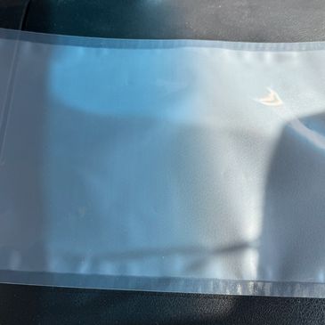 Clear plastic bag lying on a textured black surface with light reflections.
