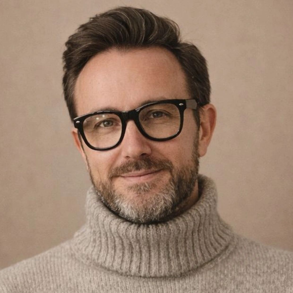 Man with glasses and a gray turtleneck sweater smiling softly.