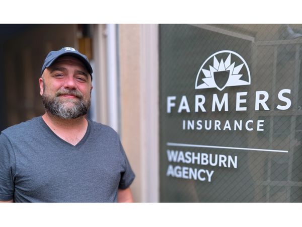 A smiling man stands next to a Farmers Insurance Washburn Agency sign.