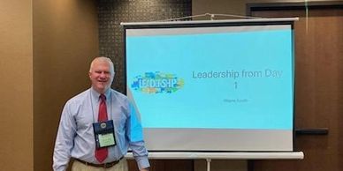 Man standing next to a presentation screen titled 'Leadership from Day 1'.