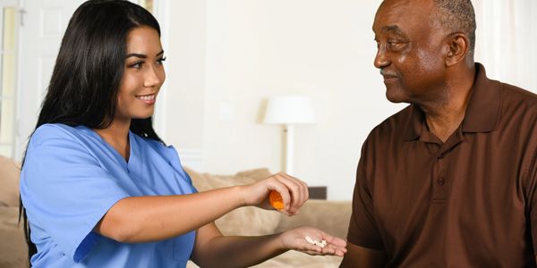 A nurse giving medication to an elderly man at home.