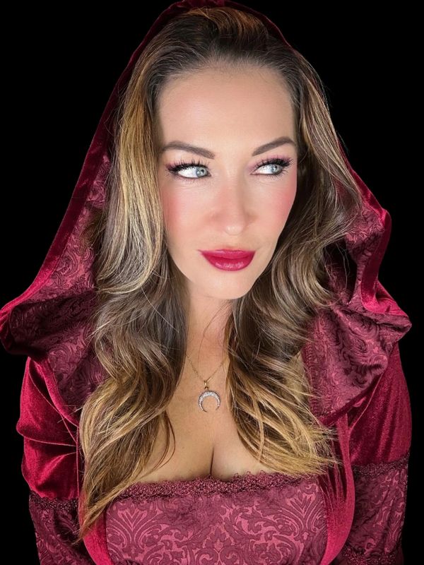 Woman in a red velvet hooded dress with striking blue eyes and red lipstick.
