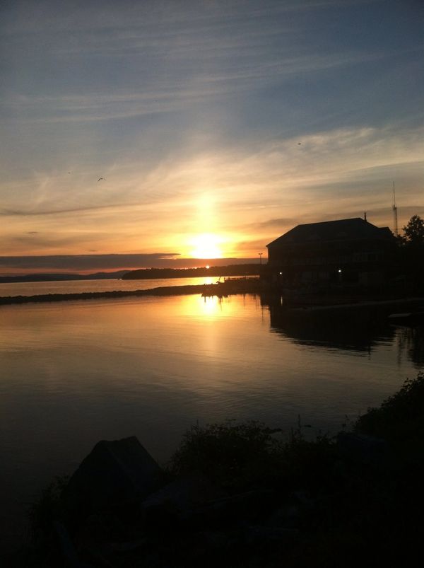 Sunset over calm water with silhouetted building and birds.