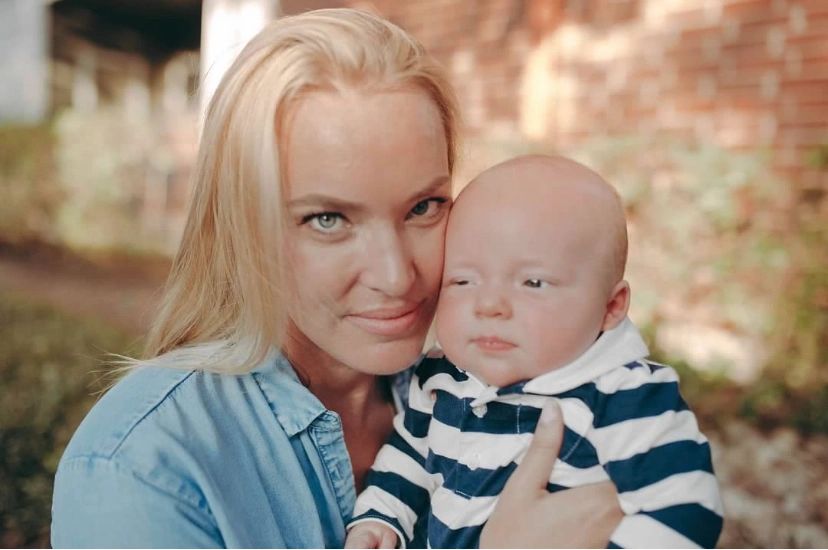 A woman lovingly holding a baby outdoors with a soft background.