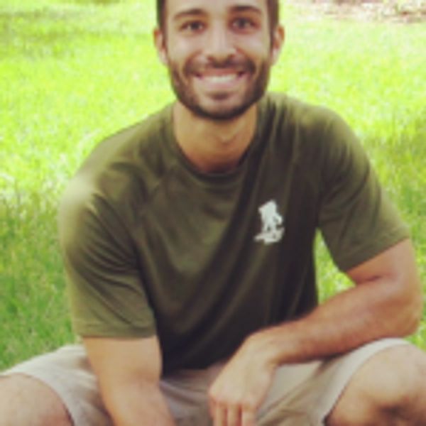 Smiling man sitting on grass in casual clothes.