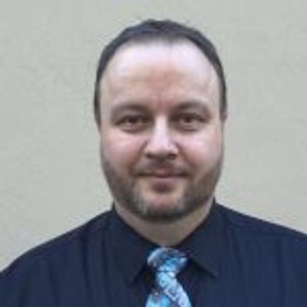 Man with beard wearing a black shirt and blue patterned tie.