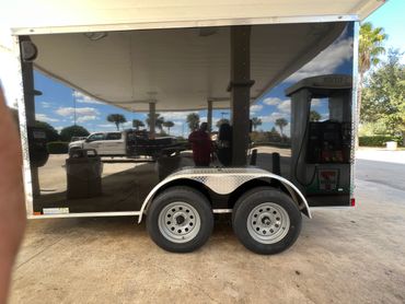 Reflective black trailer with dual wheels parked near a gas station.