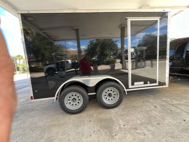 A shiny black trailer with dual wheels parked on concrete.