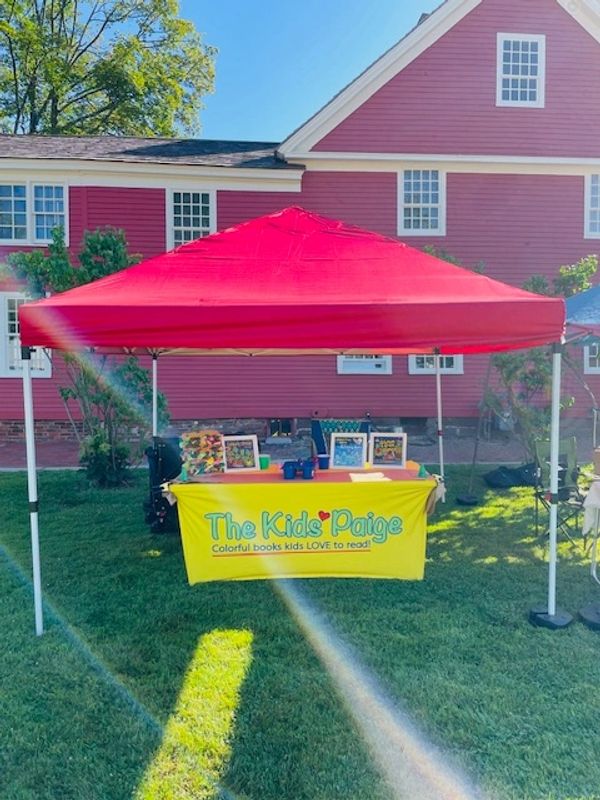 A red tent over a table with a bright yellow tablecloth that displays a giant sandwich prop and fram