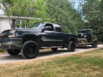 Picture of blue truck pulling an antique car in a trailer behind it.