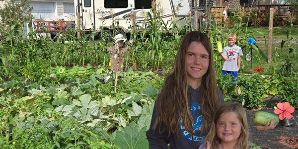 Two girls smiling in a garden with a boy in the background.