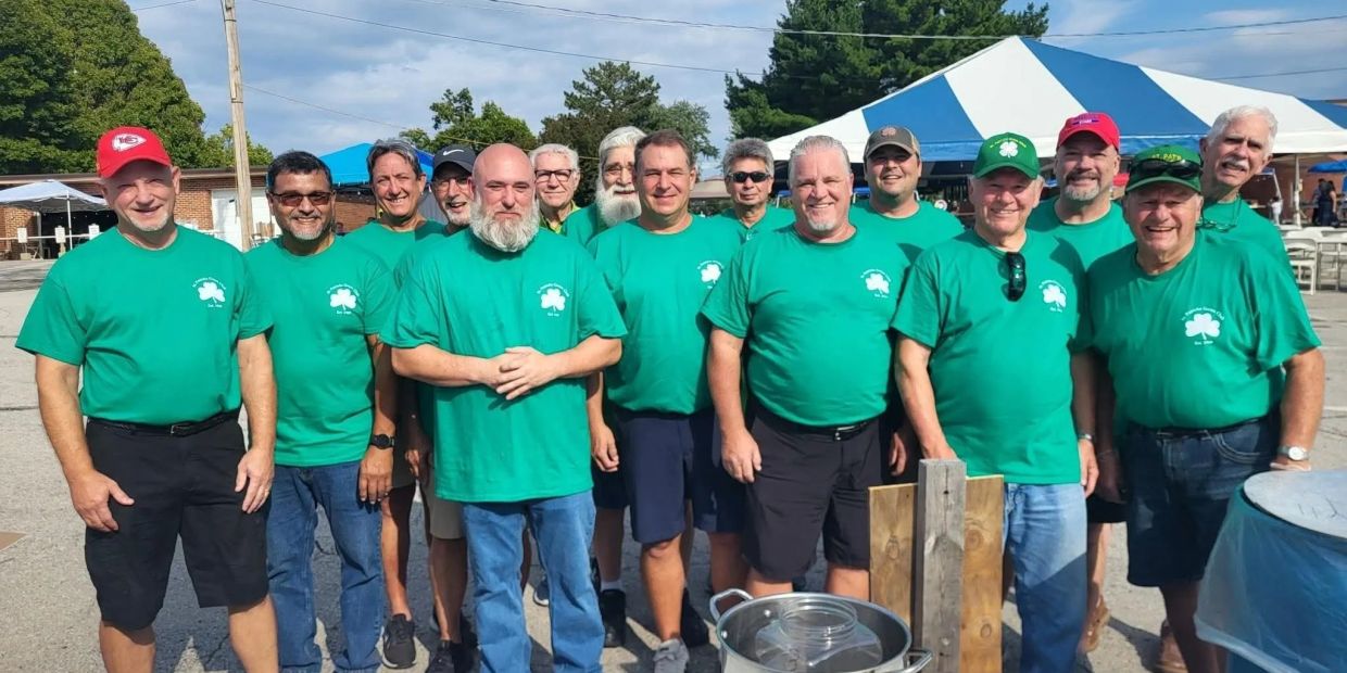 Group of men in green shirts outdoors by tents.