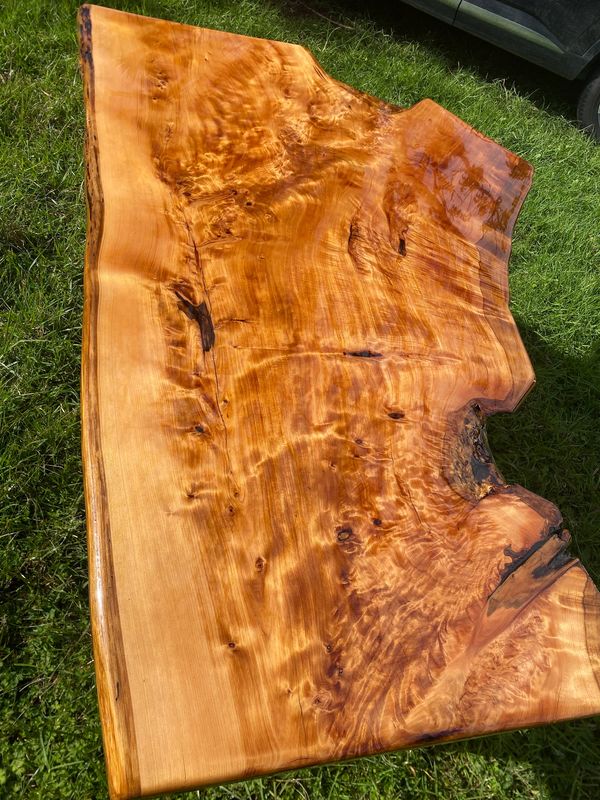A polished wooden slab with rich natural grain patterns on grass.