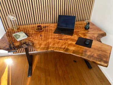 A live-edge wooden desk with a laptop, coffee cup, and book on it.
