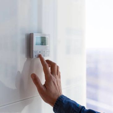 Hand adjusting a digital thermostat on a white wall.