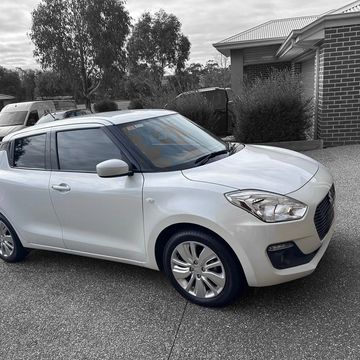 White compact car parked in a driveway next to a brick house.