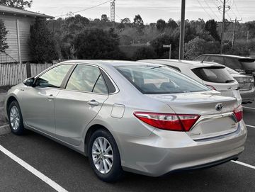 Silver Toyota Camry parked in a lot near houses and trees.