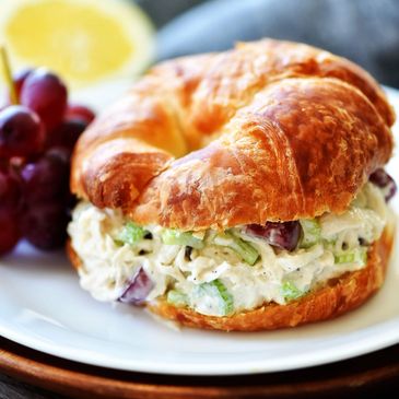 Croissant sandwich filled with chicken salad and grapes on a white plate.