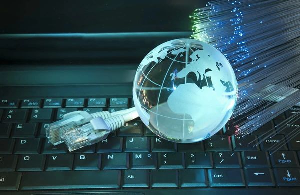 Glass globe, ethernet cable, and fiber optic strands on keyboard symbolizing global internet.