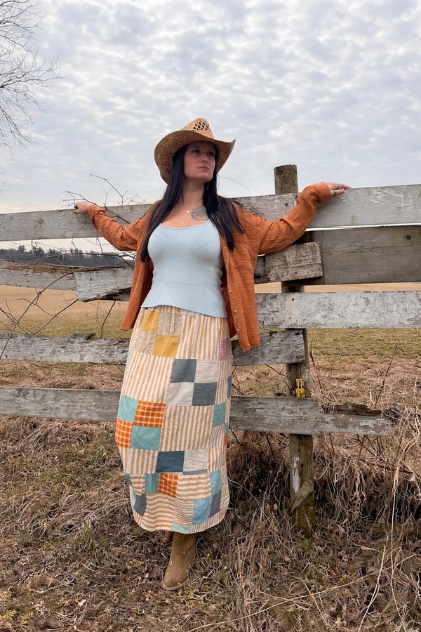 Woman in a cowboy hat leaning on a rustic wooden fence in a rural field.