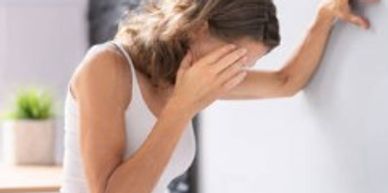 Woman leaning against wall, covering her face in distress.
