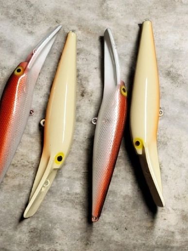 Four fishing lures with long bills in red and cream colors.