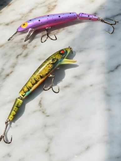 Two colorful fishing lures with treble hooks on a marble surface.