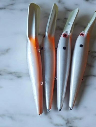 Four silver fishing lures with orange accents placed on a marble surface.
