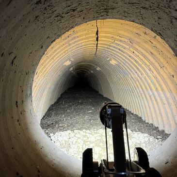 View inside a cracked, corrugated tunnel illuminated by a spotlight.