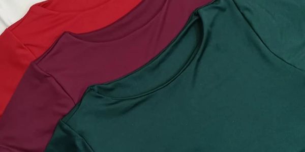 Three solid-colored t-shirts in green, maroon, and red laid out overlapping.