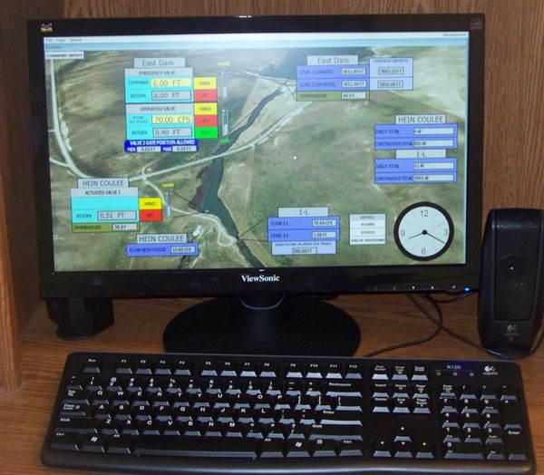 Computer screen displays East Dam and Hein Coulee water management data with keyboard and speakers.