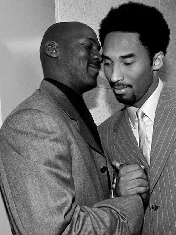 Two men in suits share a warm, close handshake in a candid moment.