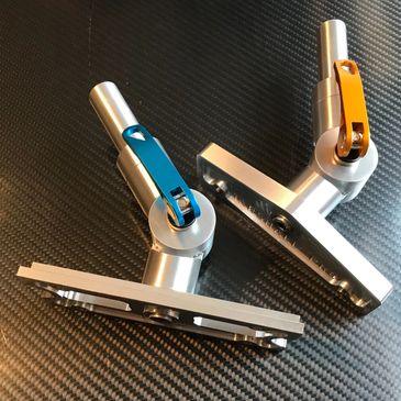 Two metallic adjustable mounts with blue and orange levers on a carbon fiber surface.