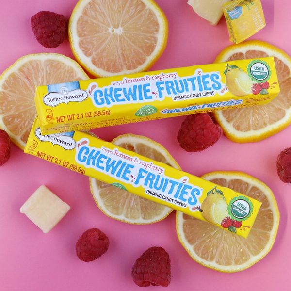 Two packs of organic lemon and raspberry Chewie Fruities with fresh lemon slices and raspberries.