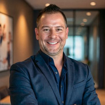 Smiling man in a navy suit standing confidently indoors.
