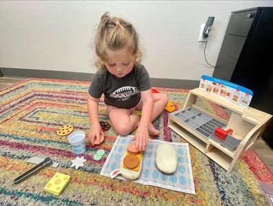 Child playing on floor with pretend sandwich shop toys during speech therapy session