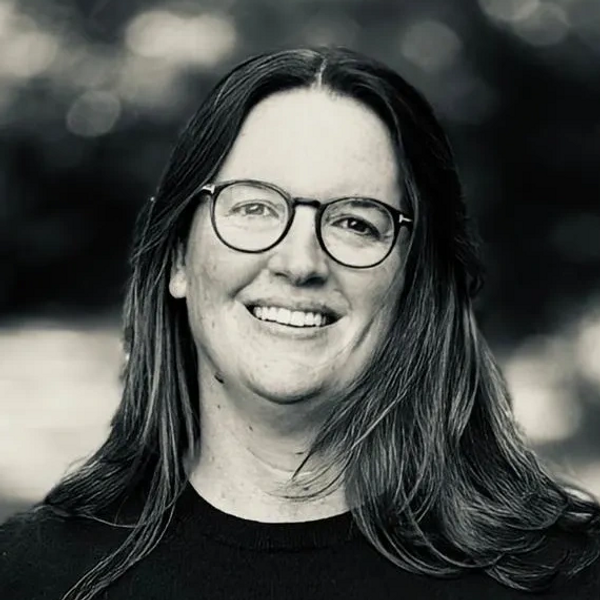 Smiling woman with glasses in a black sweater outdoors.