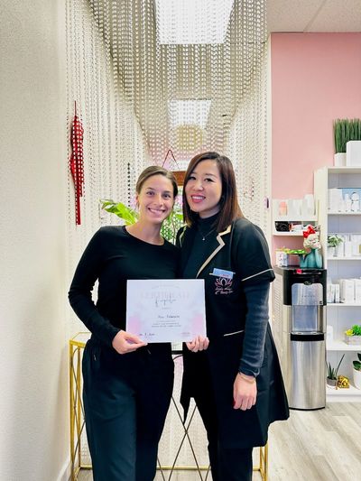 Two women smiling, one holding a certificate, standing in a bright, modern indoor space.