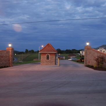 Entrance gate of a residential area at dusk with brick pillars and a small guardhouse.