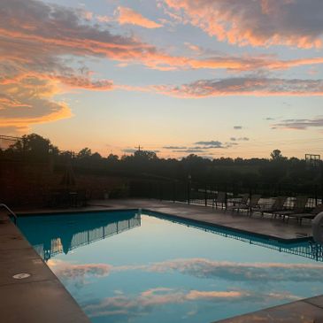 Peaceful sunset reflecting on a calm swimming pool with lounge chairs nearby.