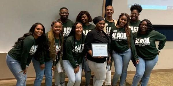 Group photo of smiling people wearing matching "BLACK Excellence" shirts.