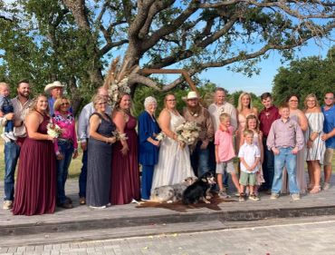 A wedding party posing outdoors with a dog lying in front.