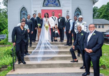 A wedding party poses on church steps with bride and groom at center.