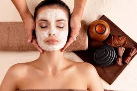 Woman receiving a facial massage with a white face mask applied.