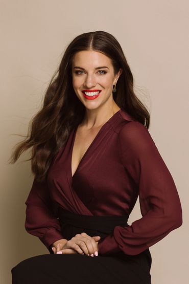 Woman with long brown hair smiling, wearing a burgundy blouse and black skirt.