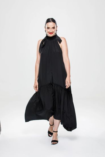 Woman in a flowing black dress and black heels, smiling confidently.