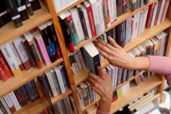 Person pulling a book from a shelf filled with various books.