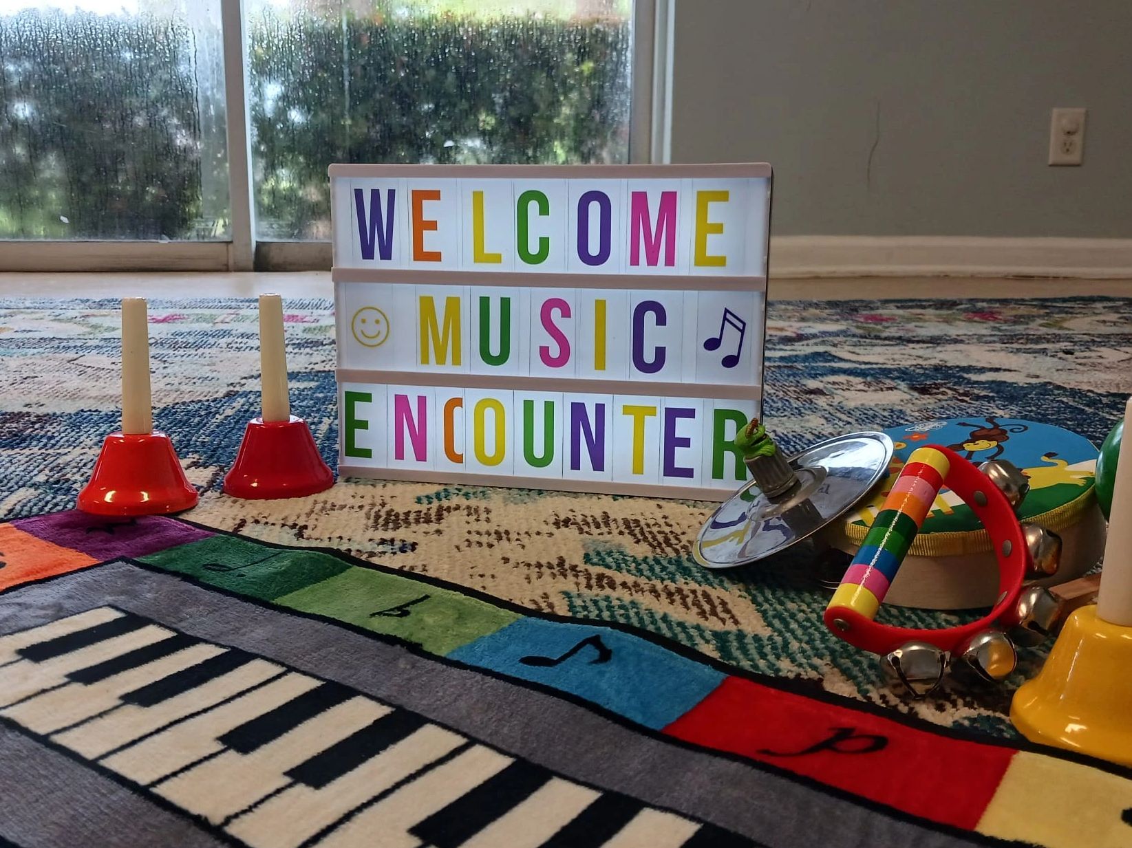 Colorful musical instruments and a sign saying 'Welcome Music Encounter' on a vibrant rug.